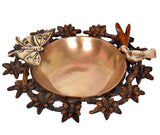 Brass urli bowl with dark floral ring and bird-and-butterfly motifs around the edge