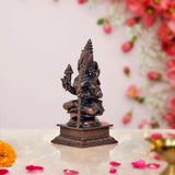 Rear view copper-tone deity sculpture with tall crown and trident, seated figure