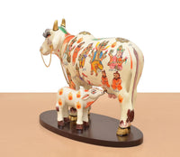 Side view of resin Kamdhenu cow with calf figure, white body and colorful people patterns