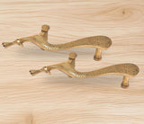 Brass peacock door handle pair on light wood, showing arched body and leaf details