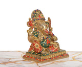 Side view of seated Ganesha brass idol with multicolor beadwork and ornate skirt details