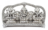 Close front depiction of silver metal Ganesha, Lakshmi & Saraswati on patterned base