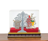 Radha-Krishna figurine in clear box with ornate tree cutout, red base, Holi decor
