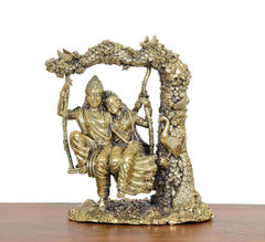 Brass Radha-Krishna idol on swing, full front view with engraved arch and base.