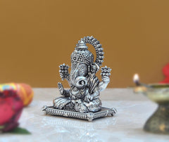 Seated Ganpati idol in brass finish, detailed jewelry and crown, front view.