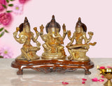 Brass-gold Lakshmi, Ganesh, and Saraswati idol with raised hands on round pedestal