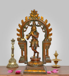 Brass Krishna idol playing flute in ornate Kirtimukha frame sculpture, 13 in height