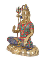 Brass Shiva sculpture in seated pose, raised hand and trident, stonework detail