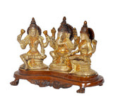Three seated Hindu deity idols: Lakshmi, Ganesh, Saraswati on brown decorative pedestal