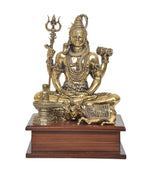 Brass Lord Shiva murti sitting with trident and drum, on dark wooden pedestal
