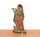 Side view of Radha Krishna brass statue, colorful patterned robes and round decorated base