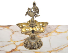 Brass peacock topper above five diya bowls on decorative oil lamp stand
