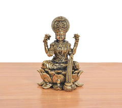 Seated Lakshmi deity idol, ornate jewelry and crown, hands raised over lotus seat