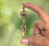 Brass dorje vajra furba with ornate top and pointed blade, held in hand