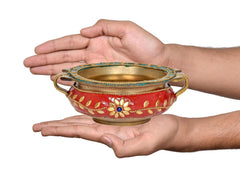 Brass urli held in hands, red enamel bowl with gold rim and blue beaded trim