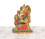 Side view brass Ganesha idol with jeweled red-and-green garments, trunk, and halo backdrop