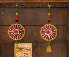 Two latkans toran on wall: orange-and-white round discs with pink center, colorful bead tassels, bells