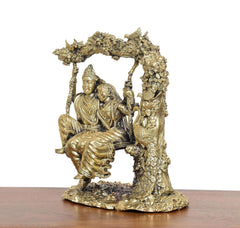 Brass Radha-Krishna idol on swing, back/three-quarter view of seated figures.