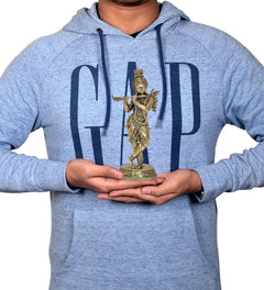 Brass Lord Krishna idol held in hands, small gold-toned figure on round base.