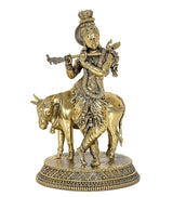 Brass Krishna on cow statue, frontal view, flute in hand, decorative crown and jewelry