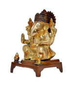 Brass Ganesha statue, side view on wooden pedestal, golden ornaments