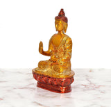 Brass Buddha idol side view, hand raised in Abhaya mudra, ornate golden robe, lotus base