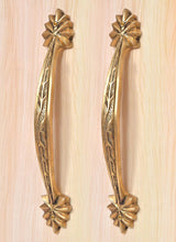 Golden brass door handle pair with engraved leaf pattern and four-petal rosette accents at ends.