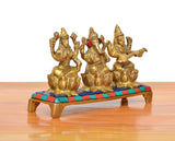 Side view of golden brass idol trio: Lakshmi, Ganesha and Saraswati on colorful base