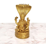 Golden brass Vishnu seated with Lakshmi, raised hands, serpent hood behind