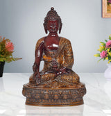 Meditating Buddha statue with dark red face and gold textured robe, seated on pedestal