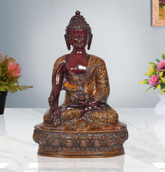 Meditating Buddha statue with dark red face and gold textured robe, seated on pedestal