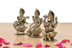 Three-quarter view of brass seated Lakshmi, Saraswati and Ganesha on lotus bases.