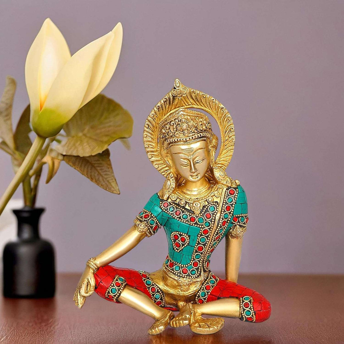 Brass Indra Devta statue, seated cross-legged in teal and red jeweled outfit, golden face.