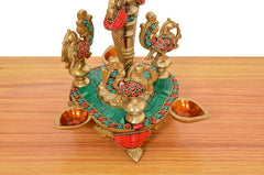 Brass peacock diya stand base with green enamel, red details, and side oil cups