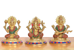 Three seated brass deities—Lakshmi, Ganesh and Saraswati—front view with multicolor details