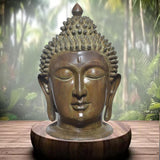 Brass Buddha head statue on round base, closed-eye details and textured hair curls