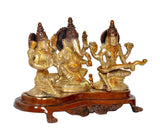 Lakshmi and Ganesh seated beside Saraswati brass-gold statue on round brown platform