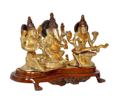Lakshmi and Ganesh seated beside Saraswati brass-gold statue on round brown platform