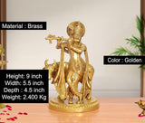 Golden brass Krishna with flute held forward, standing beside cow idol