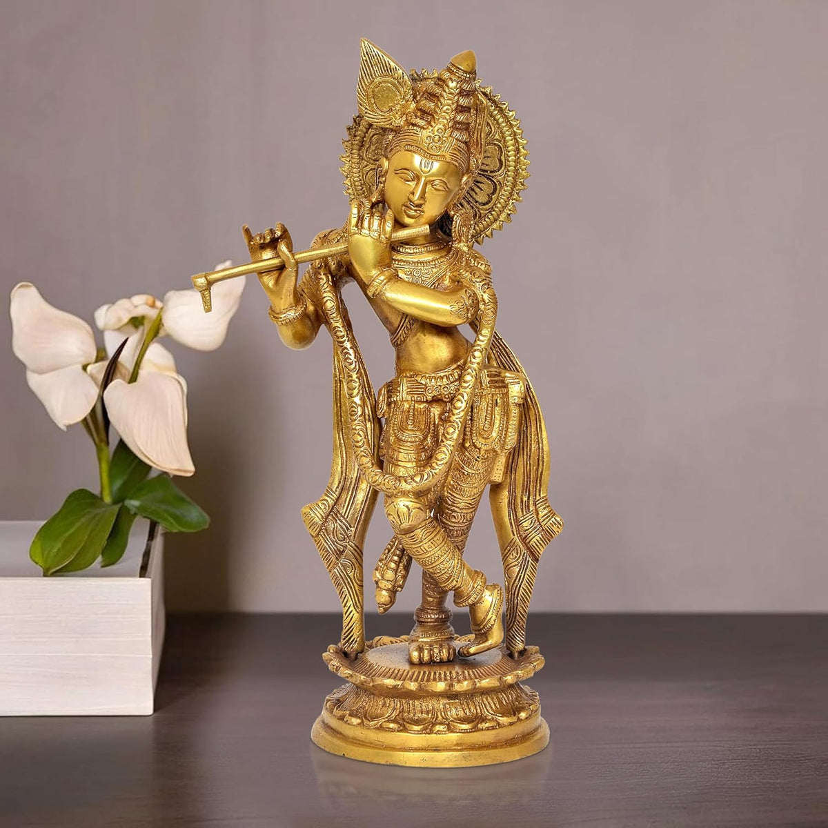 Brass Krishna idol statue holding flute, ornate crown and halo, on round pedestal