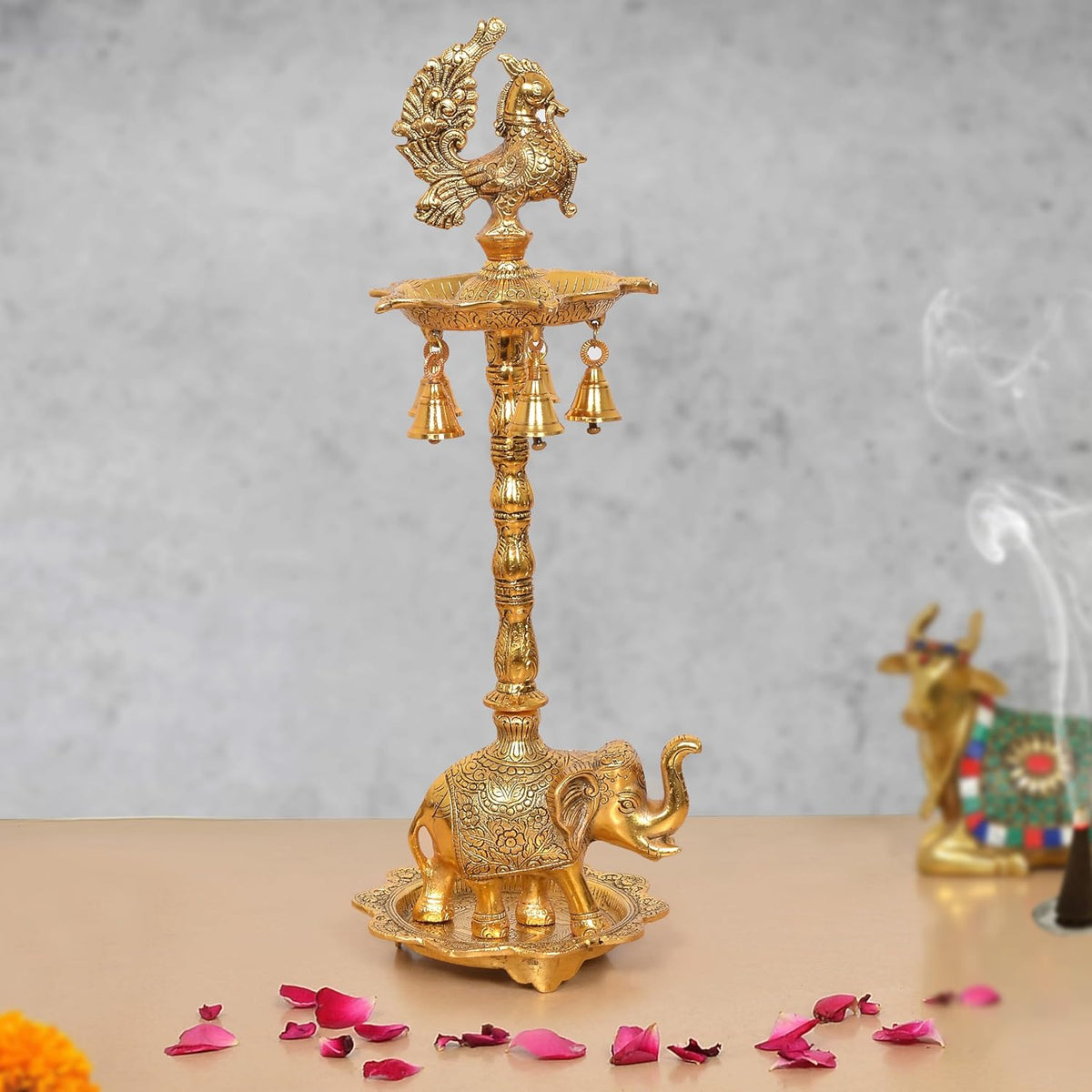 Golden metal peacock oil lamp stand with elephant base and tiered oil bowl