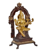 Seated Saraswati brass idol shown from angle, ornate arch and sculpted halo