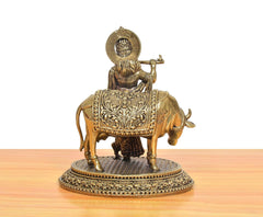 Brass Krishna playing flute on cow idol, ornate back panel and engraved base