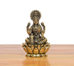 Front view bronze Lakshmi statue sitting on lotus petals, crown details and layered jewelry.