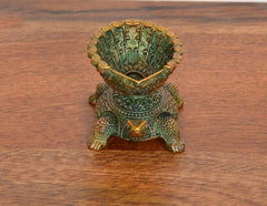 Close-up of brass tortoise oil lamp diya, fan-shell top and textured green body