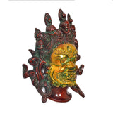 Brass Mahakala wall hanging mask, angled view with gold face and red-green accents