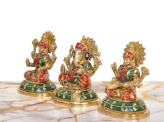 Three brass idols with multicolor ornamented dresses, each with raised arms and halo.