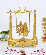 Brass Radha-Krishna swing idol on ornate base with hanging chains and peacocks