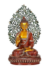 Seated golden Buddha statue with red robe, raised hand, green leaf tree canopy