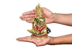 Hands holding brass Krishna statue, multicolor seated idol with flute, 8 inch